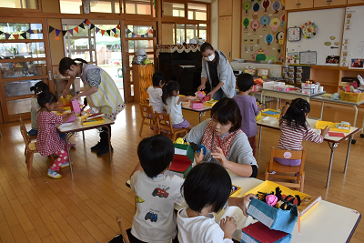 エプロンを着用した女性に教えてもらい作業する園児たちの写真