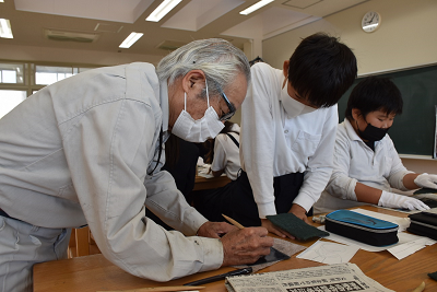 銅板に書き込む男性を見ている男子児童の写真