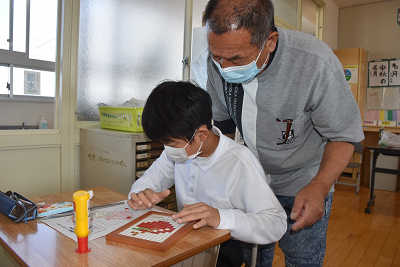 タイルでリンゴ模様を作る男子児童を後ろから見守る男性の写真