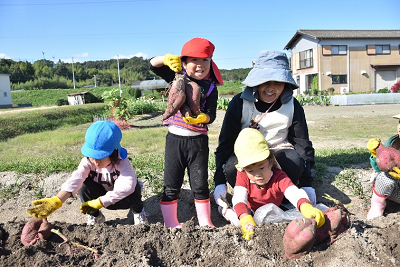 堀ったサツマイモを持って立ち笑顔を見せる園児の写真