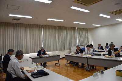 ロの字型に向き合いそれぞれに配膳された給食を食べるスーツ姿の人々の写真