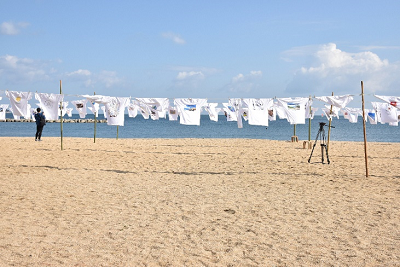 様々なデザインのTシャツが何列も飾られた浜辺の写真