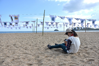 浜辺に座りカメラを見る少女の写真