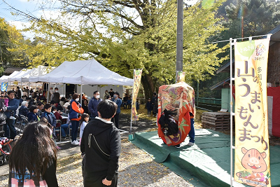 のぼりが飾られたステージで披露されている獅子舞を見る人々の写真