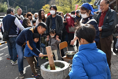 人々に囲まれて、親子が一緒に杵を持ち餅をついている写真
