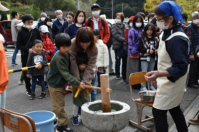 臼に入った緑色の餅をつく親子の写真