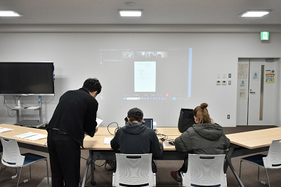 スクリーンの前で話し合う3人の後ろ姿の写真