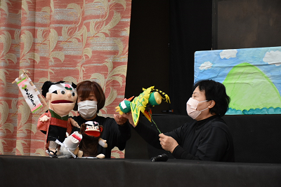 女性二人が少年とイヌ、サル、キジの人形を動かしている写真