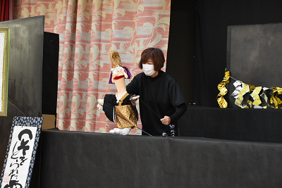 袈裟を着た人形を動かす女性の写真