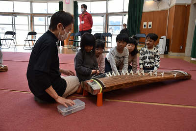 琴の前で一列に座り、琴を眺める子供の写真