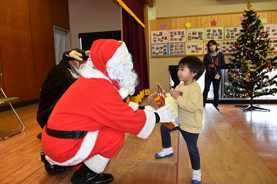 しゃがんだサンタクロースからプレゼントを受け取る園児の写真