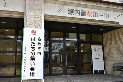 「さぬき市 はたちの集い会場」と書かれた看板が建物入口に設置されている写真
