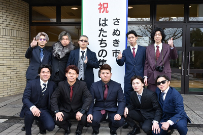 看板の前でスーツを着用した男性が二列に並んでいる写真