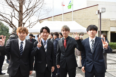 スーツ姿の男性4人が一列でピースサインしている写真