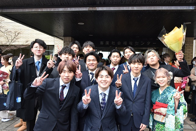 建物の前でスーツ姿の男性や振り袖姿の女性が集まっている写真