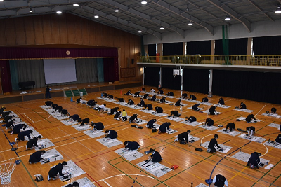 体育館で書初めをしている児童たちの写真