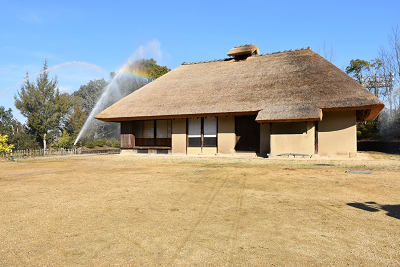 茅葺き屋根の古民家に向かって、スプリンクラーから放水が行われている写真