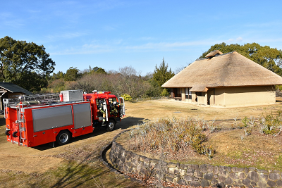 茅葺き屋根の古民家前の庭に消防車が停まっている写真