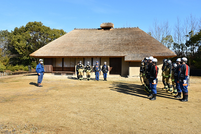茅葺き屋根の古民家前で消防団員たちが整列している写真