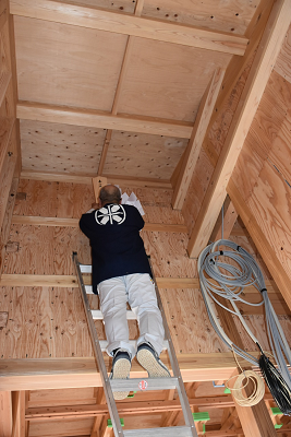 梯子に上り、神棚に札を飾る男性の後ろ姿の写真