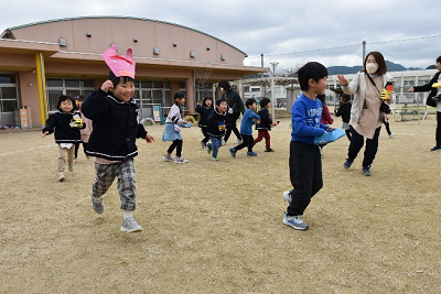 手作りの鬼のお面をつけた園児や豆を持った園児が広場を走っている写真