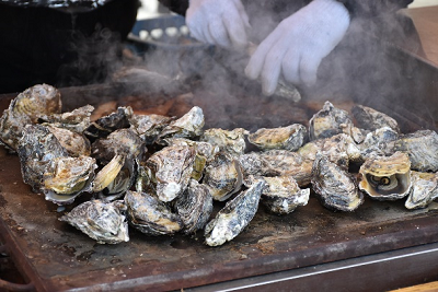 鉄板で焼かれた殻付き牡蠣が湯気を立てている写真