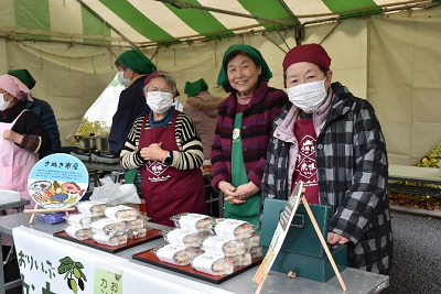 品物が並んだ机の前に立つ女性3人の写真