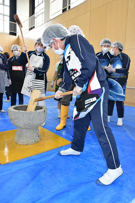 ジャージにエプロンを着用した男子児童が餅をついている写真