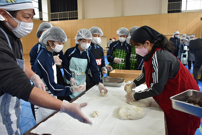 児童たちが囲む台で餅を細かく分けていく女性の写真