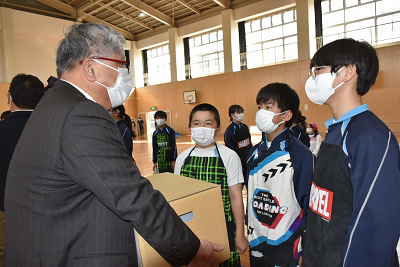 箱を持つスーツ姿の男性と話す児童3人の写真