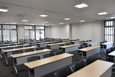 1つの長机に3脚の椅子で横3列縦6列に配置された室内の写真