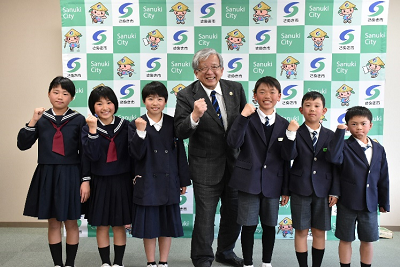 生徒達と男性が並んでガッツポーズをとっている写真