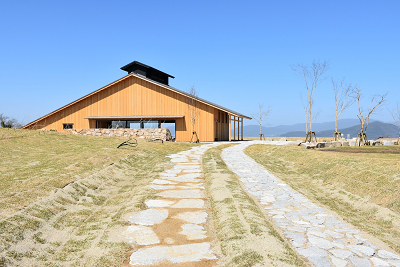 木造の建物へ石畳の小道が続き、背後に山並みが広がっている写真