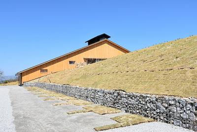 芝生の法面と石積みの擁壁の奥に建つ木造建築物の写真