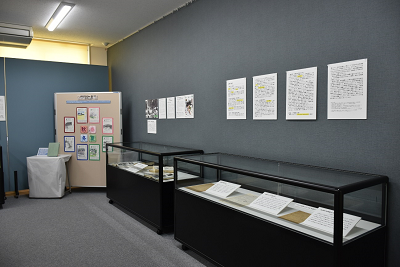 解説パネルが貼られた壁の下に、資料が展示されたガラスケースが設置されている写真