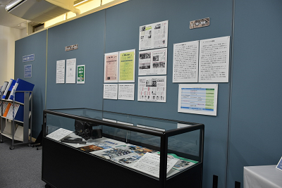 資料が展示されたガラスケースと解説パネルが貼られた壁の写真