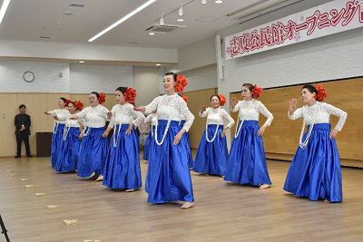 青いスカートを着て、頭に赤い花飾りをつけた女性たちがフラダンスを踊っている写真