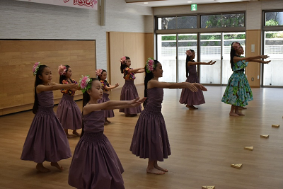 頭に花飾りをつけた子供たちが両手を前に出してフラダンスを踊っている写真