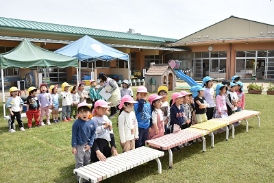 広場でベンチ前に列になって並ぶ園児たちの写真