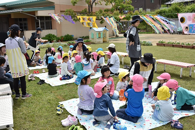 広場にレジャーシートを広げて座る園児たちの写真
