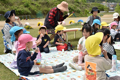レジャーシートに座り、お菓子を食べる園児たちの写真