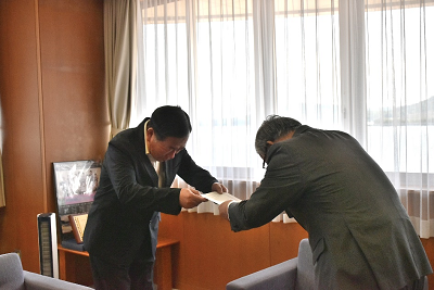 スーツ姿の男性2人が向かい合って書類を受け渡している写真
