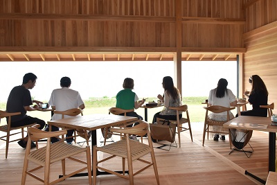 2人ずつテーブルに座って食事をする男女6人の後ろ姿の写真