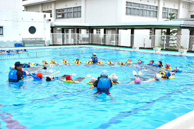 大人数の児童がライフジャケット着用で、円状に手をつないで水面に浮かぶ写真