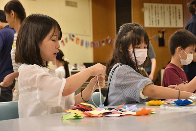 紙と紐を使い作業を行う2人の女子児童の写真