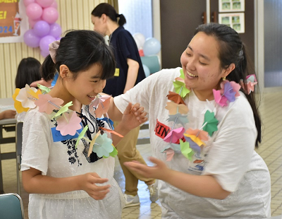 花の形の紙を紐に通して首飾りにしたものを身に付ける女子児童の写真
