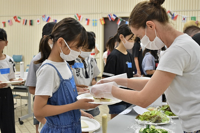 児童が持つお皿にサンドイッチを置く女性の写真