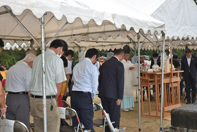 紙を持って読んでいる神主に頭を軽く下げている大人達の写真