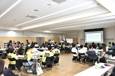 大勢の人がグループで座ってスクリーンを見ている写真