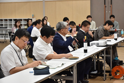 並んで座っている中でマイクをもって話している男性の写真